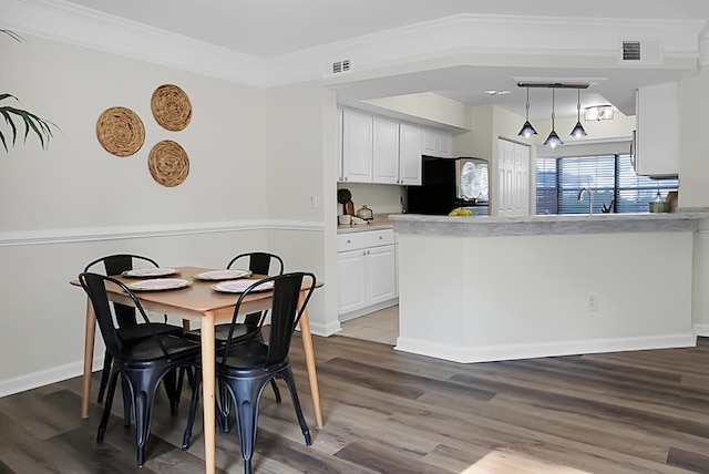 kitchen with pendant lighting, white cabinetry, hardwood / wood-style flooring, stainless steel refrigerator, and crown molding