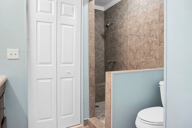 bathroom with ornamental molding, vanity, toilet, and tiled shower