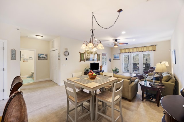 dining space with ceiling fan with notable chandelier and light colored carpet