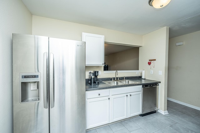 kitchen featuring dark countertops, appliances with stainless steel finishes, white cabinetry, a sink, and baseboards