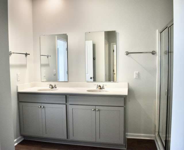 full bathroom with a sink, baseboards, a shower stall, and double vanity