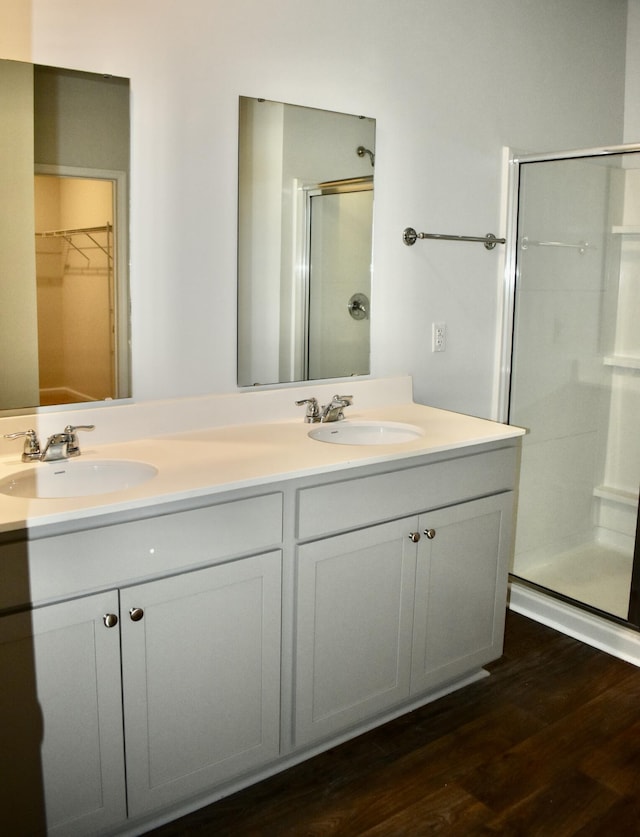 full bathroom with double vanity, wood finished floors, a stall shower, and a sink