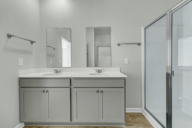 full bathroom with double vanity, wood finished floors, a stall shower, and a sink