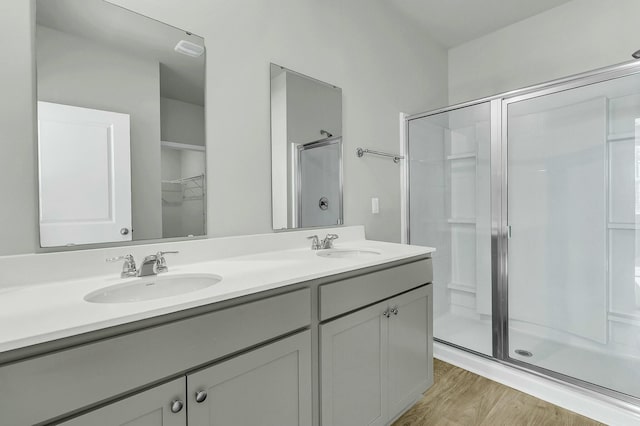 full bath with a sink, double vanity, wood finished floors, and a shower stall