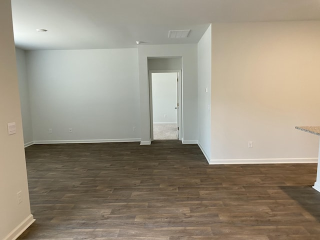 empty room featuring dark wood-style floors, visible vents, and baseboards