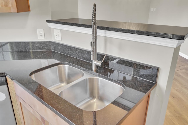 details featuring light brown cabinetry, sink, light hardwood / wood-style flooring, dark stone countertops, and dishwasher