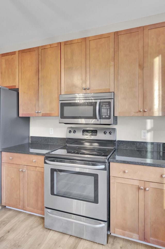 kitchen with dark stone counters, appliances with stainless steel finishes, and light hardwood / wood-style flooring