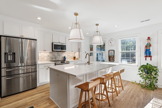 kitchen featuring white cabinetry, sink, stainless steel appliances, an island with sink, and pendant lighting