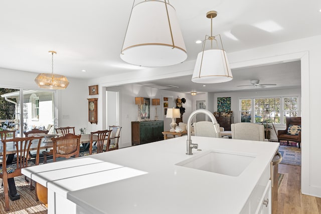 kitchen with white cabinetry, sink, light hardwood / wood-style flooring, pendant lighting, and ceiling fan with notable chandelier