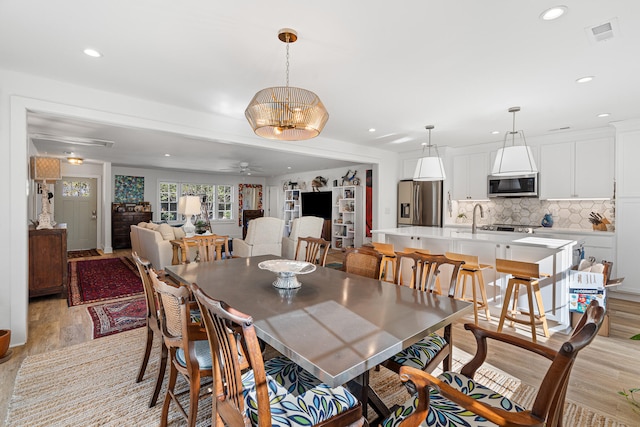 dining space featuring light hardwood / wood-style flooring, ceiling fan with notable chandelier, and sink