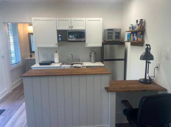 kitchen featuring kitchen peninsula, appliances with stainless steel finishes, sink, light hardwood / wood-style flooring, and white cabinets