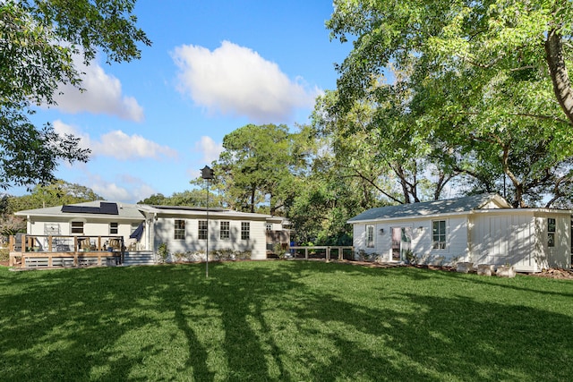 rear view of house with solar panels, a yard, and a wooden deck