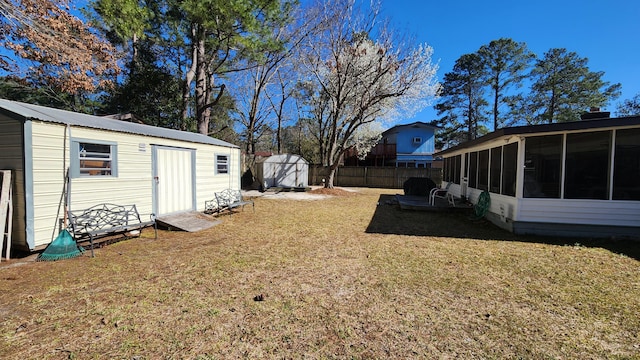 view of yard featuring an outbuilding, a shed, fence, and a sunroom