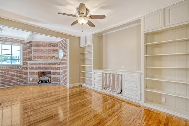 unfurnished living room featuring built in shelves, light hardwood / wood-style floors, brick wall, and ceiling fan