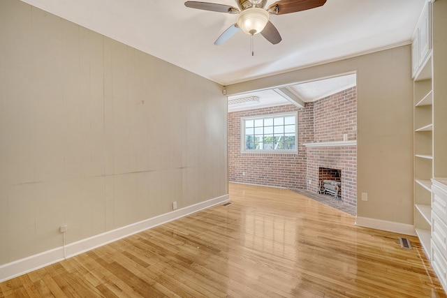 unfurnished living room with a brick fireplace, light wood-type flooring, brick wall, and ceiling fan