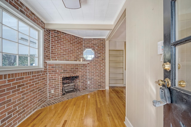 unfurnished living room with a brick fireplace, hardwood / wood-style flooring, brick wall, and crown molding