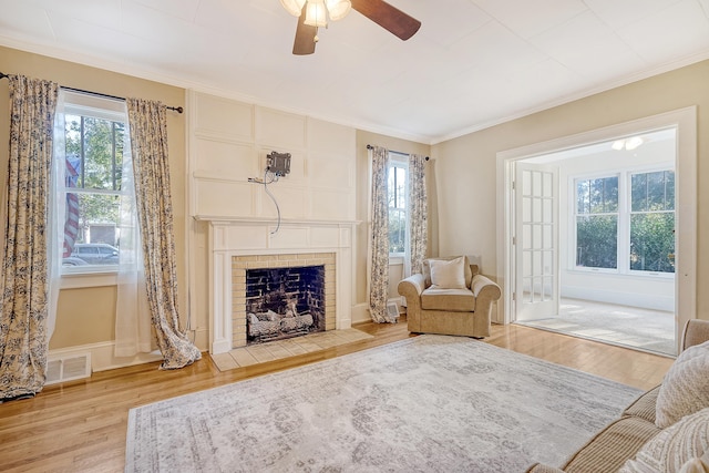 living area with ornamental molding, light wood-type flooring, a tiled fireplace, and ceiling fan