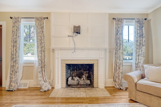 sitting room with a wealth of natural light, wood-type flooring, crown molding, and a brick fireplace