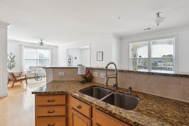 kitchen featuring crown molding, light hardwood / wood-style flooring, sink, and dark stone counters