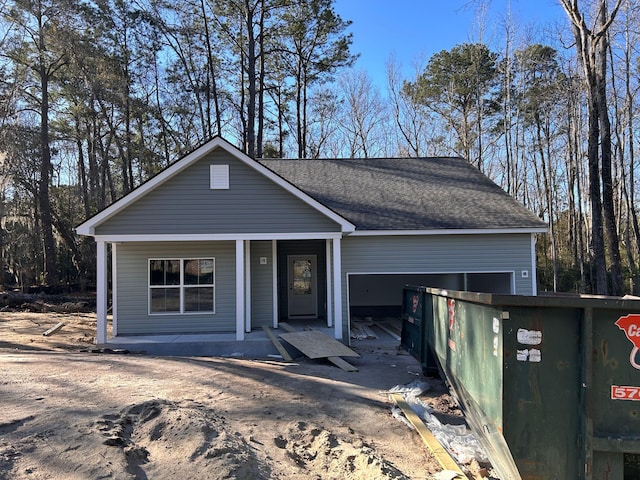 view of front of house featuring dirt driveway, roof with shingles, a porch, and an attached garage