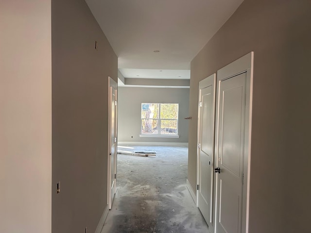 hallway with unfinished concrete floors and baseboards