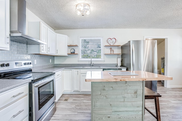 kitchen with a kitchen bar, stainless steel appliances, wall chimney range hood, white cabinets, and a kitchen island