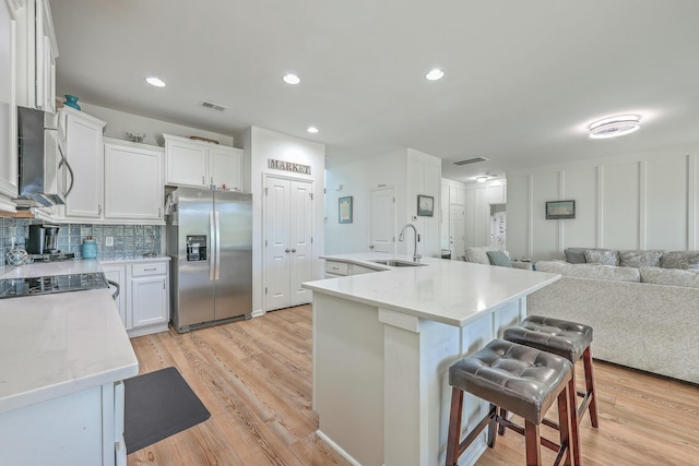 kitchen with light wood-type flooring, a kitchen island with sink, stainless steel fridge, sink, and white cabinets