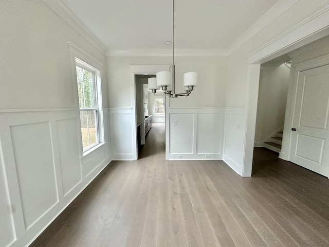 unfurnished dining area featuring crown molding, wood-type flooring, and a chandelier