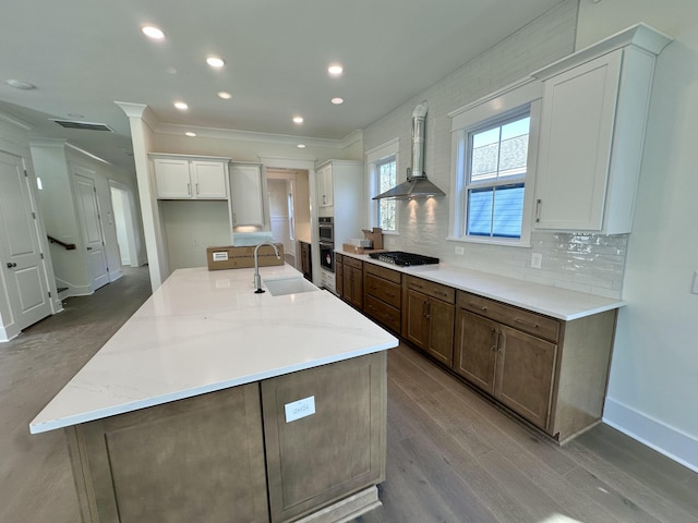 kitchen featuring a kitchen island with sink, wall chimney range hood, sink, and white cabinets