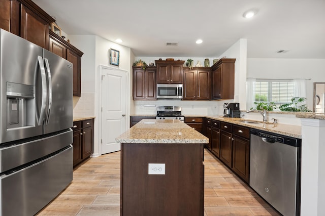 kitchen featuring stainless steel appliances, a kitchen island, light wood finished floors, a sink, and dark brown cabinetry