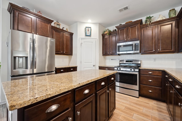 kitchen featuring appliances with stainless steel finishes, light wood finished floors, decorative backsplash, dark brown cabinets, and light stone counters