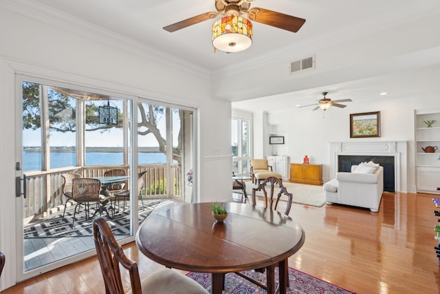 dining area with a water view, wood-type flooring, a fireplace, and ornamental molding