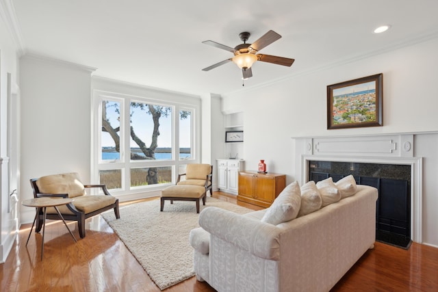 living room featuring hardwood / wood-style floors, a water view, ceiling fan, ornamental molding, and a fireplace