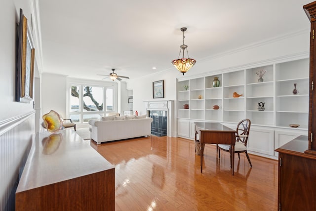 living room with ceiling fan, light wood-type flooring, crown molding, and built in shelves