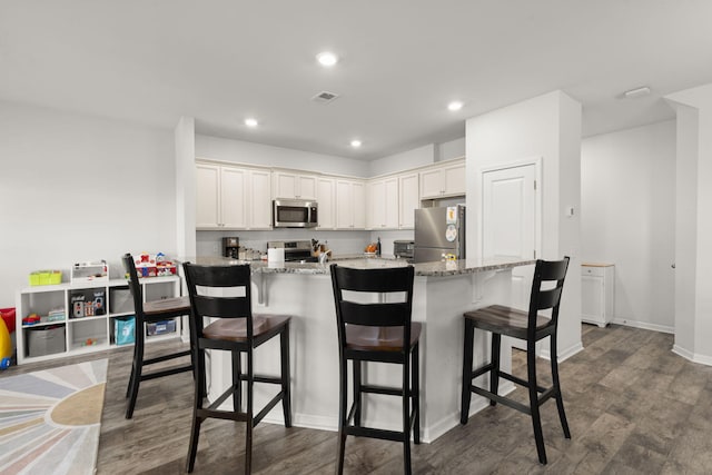 kitchen featuring visible vents, a breakfast bar, light stone counters, dark wood finished floors, and appliances with stainless steel finishes