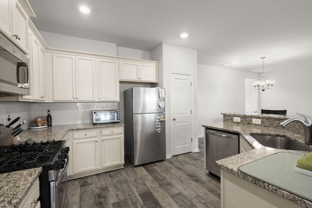 kitchen featuring dark wood-style floors, tasteful backsplash, a sink, appliances with stainless steel finishes, and a notable chandelier