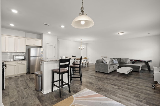kitchen featuring visible vents, freestanding refrigerator, open floor plan, a breakfast bar area, and dark wood-style floors