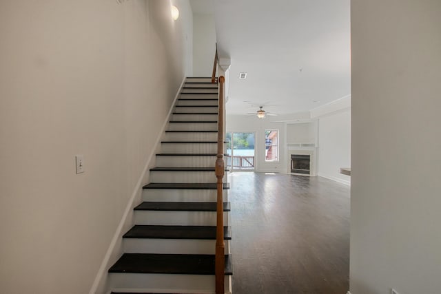 stairs with wood finished floors, a tile fireplace, baseboards, and ceiling fan