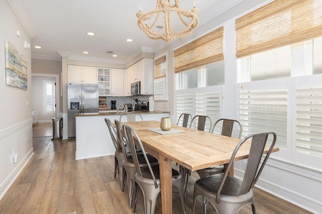 dining space with recessed lighting, wood finished floors, ornamental molding, and wainscoting