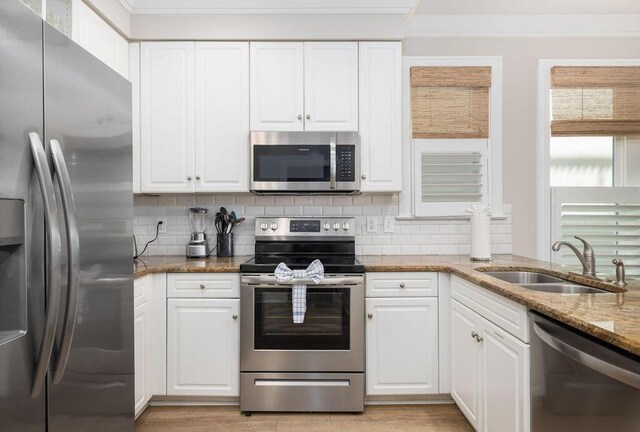 kitchen with backsplash, appliances with stainless steel finishes, white cabinetry, and a sink