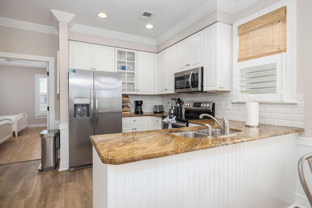 kitchen with visible vents, light stone countertops, a peninsula, stainless steel appliances, and a sink