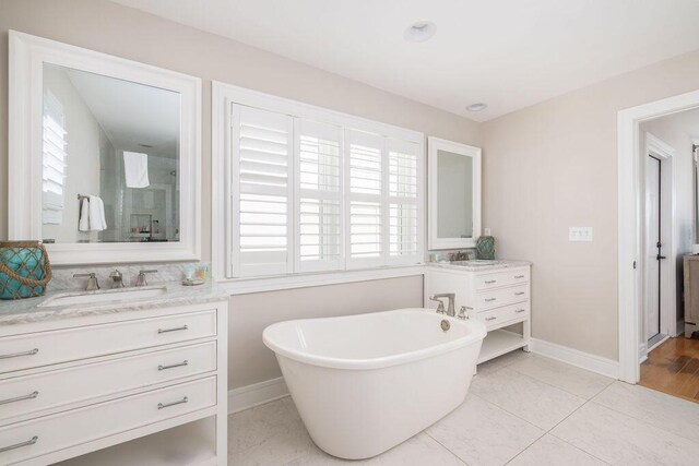 bathroom with a freestanding tub, two vanities, a sink, tile patterned flooring, and baseboards