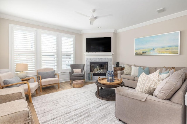 living area featuring wood finished floors, visible vents, a fireplace, ceiling fan, and crown molding