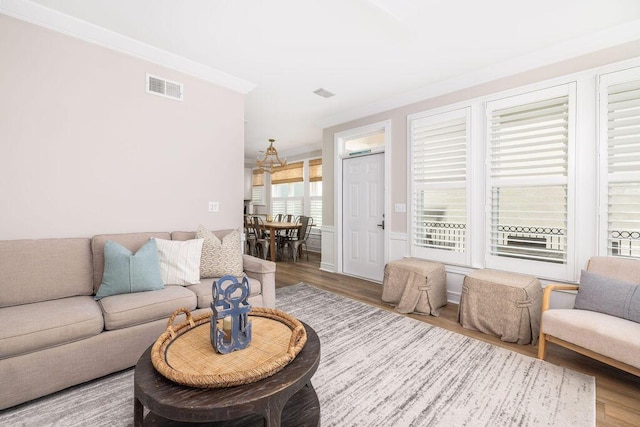 living area with wood finished floors, visible vents, and ornamental molding