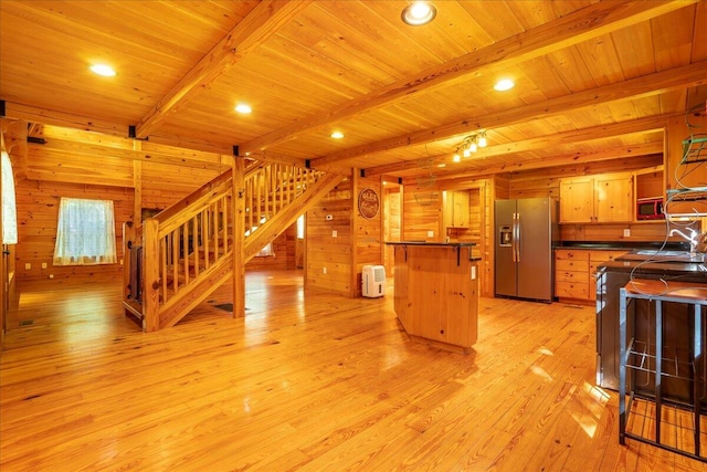 kitchen with beam ceiling, wood walls, appliances with stainless steel finishes, and light hardwood / wood-style flooring