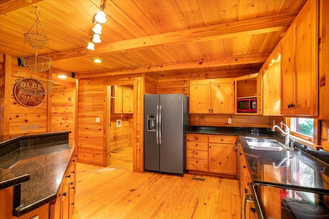 kitchen featuring wooden walls, stainless steel refrigerator with ice dispenser, black microwave, sink, and light hardwood / wood-style floors