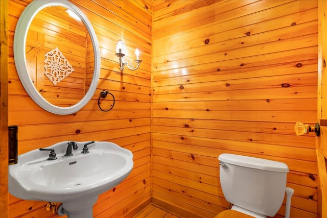 bathroom with toilet, wooden walls, and sink