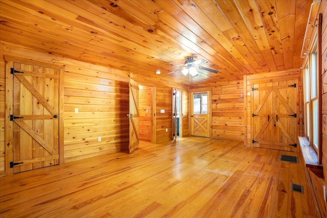 bonus room featuring wooden ceiling, a barn door, ceiling fan, light wood-type flooring, and wood walls