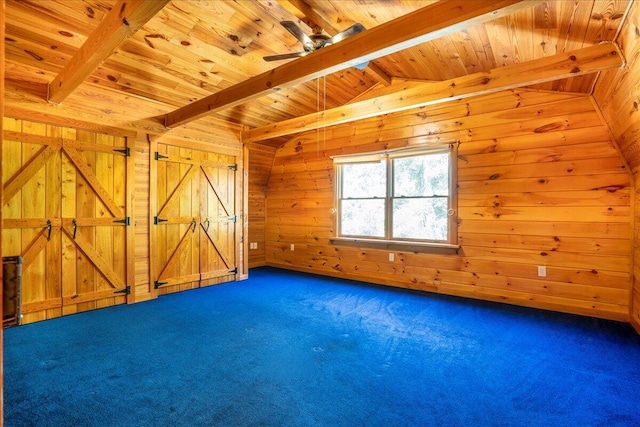 additional living space with dark colored carpet, wooden walls, wooden ceiling, a barn door, and ceiling fan