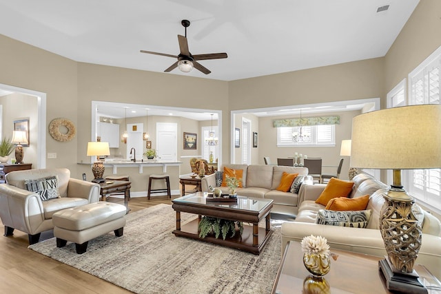 living room featuring sink, light hardwood / wood-style floors, and ceiling fan with notable chandelier